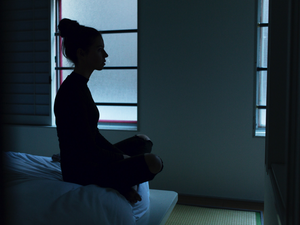 Woman sitting on the bed in the dark having a mental health crisis.