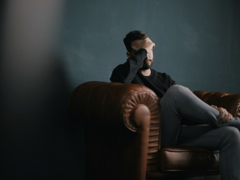 Man sitting in chair with hand over eyes looking fatigued.